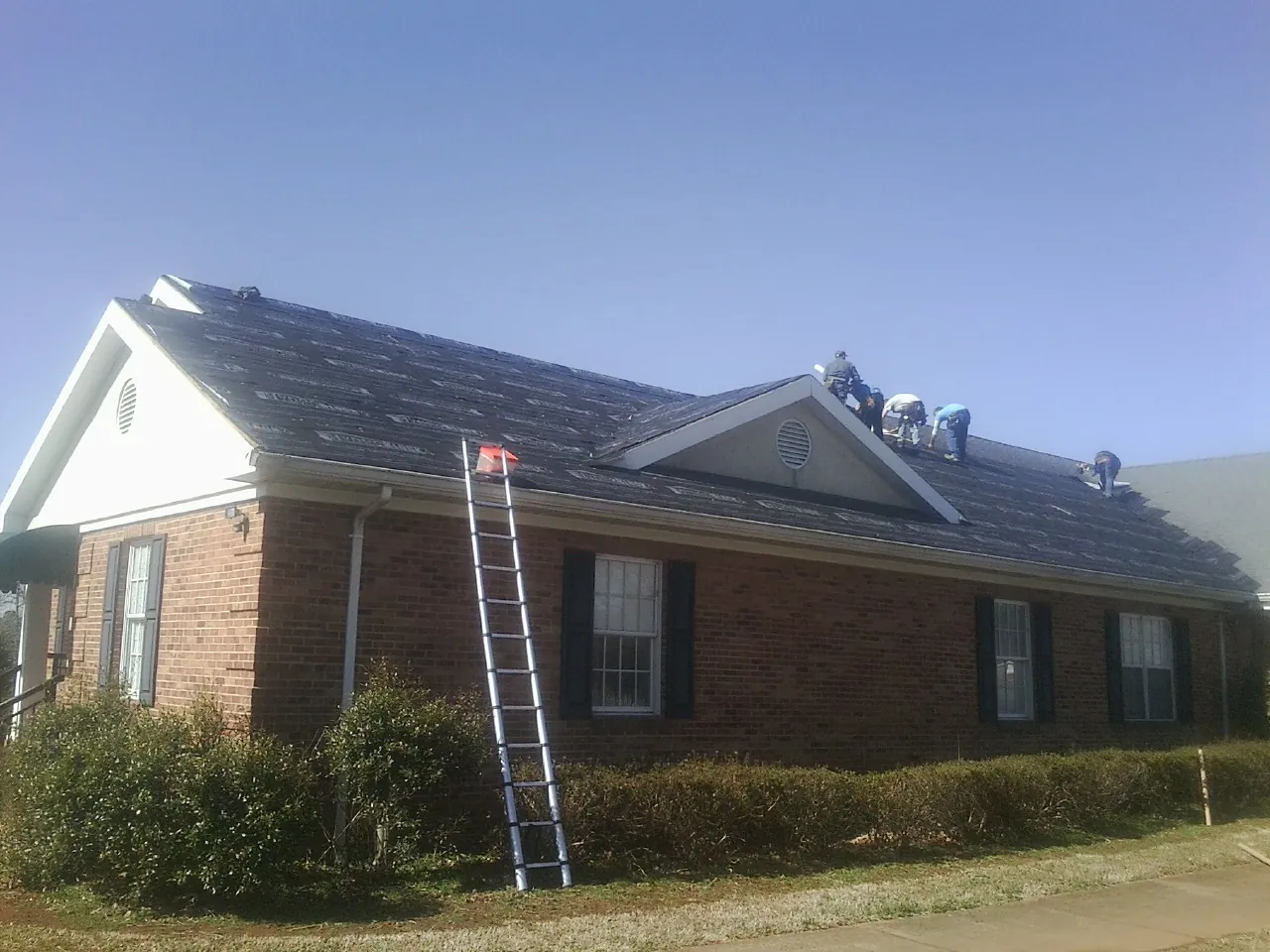 Crew tearing shingles off a brick ranch roof with a ladder set — Metal Roof Repair work by our crew in Wheeling